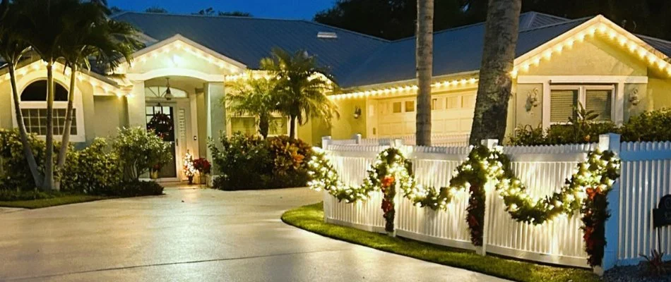 White commercial-grade Christmas lights on a home and white fence in New Smyrna Beach, FL.