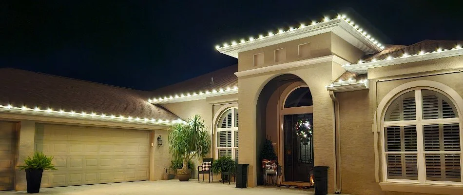 White commercial-grade holiday lights on a home in New Smyrna Beach, FL, with a garage on the side and a wreath on the door.